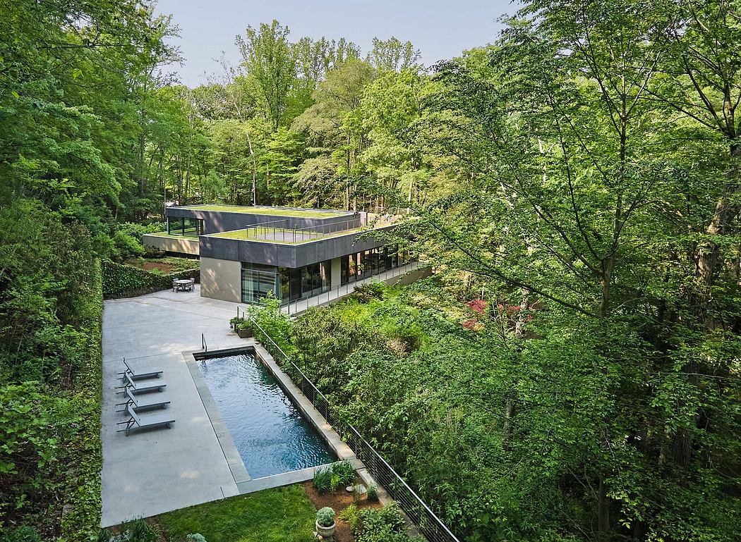A modern, minimalist house nestled in a lush, verdant forest with a sleek, rectangular pool.