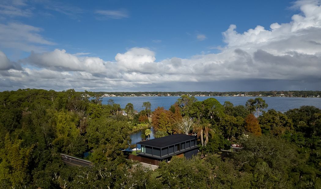 Scenic lakefront house with a black-roofed structure nestled among lush green foliage.