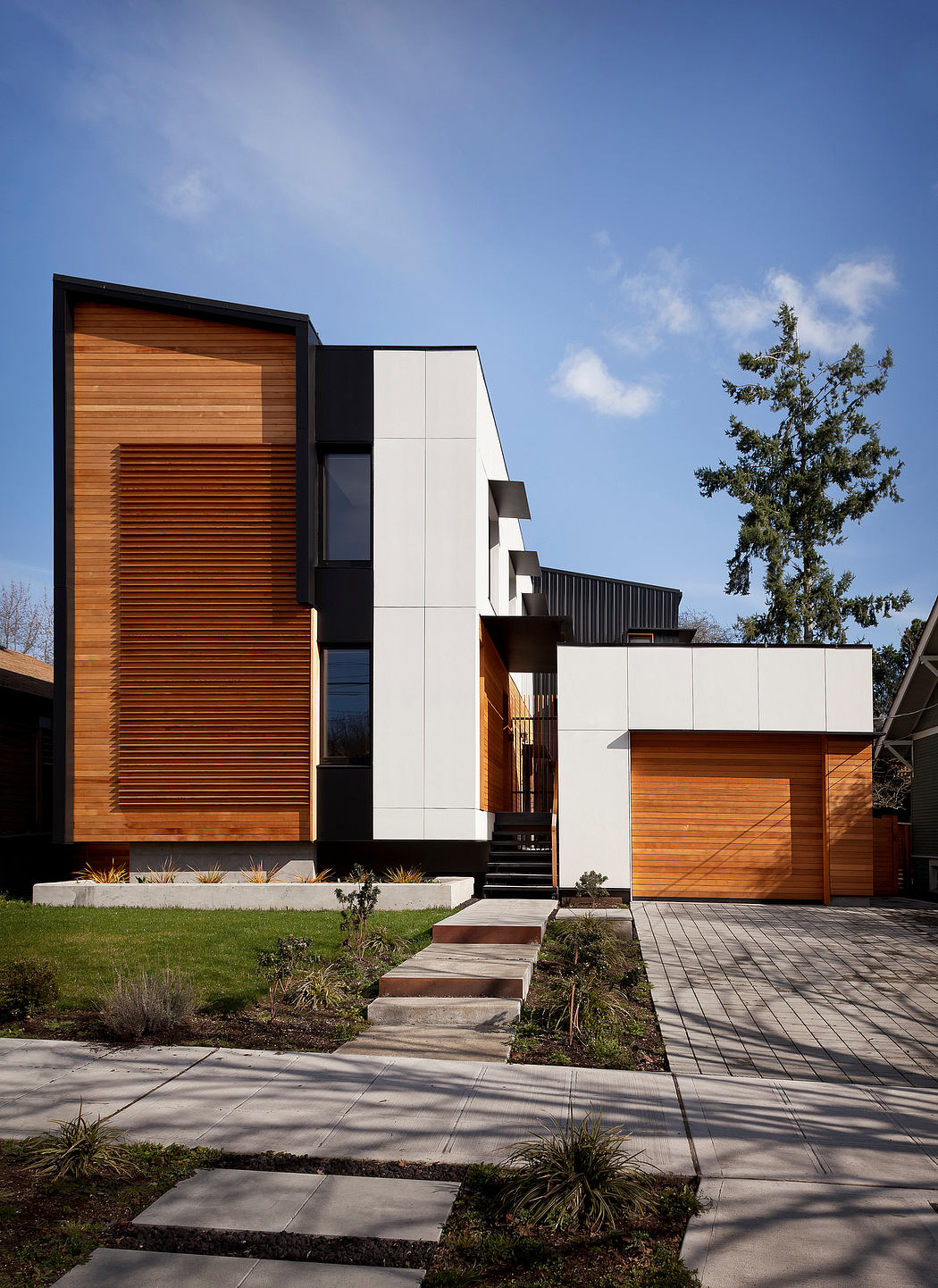 Modern two-story home with wood panels, white walls, and stepped entry path.