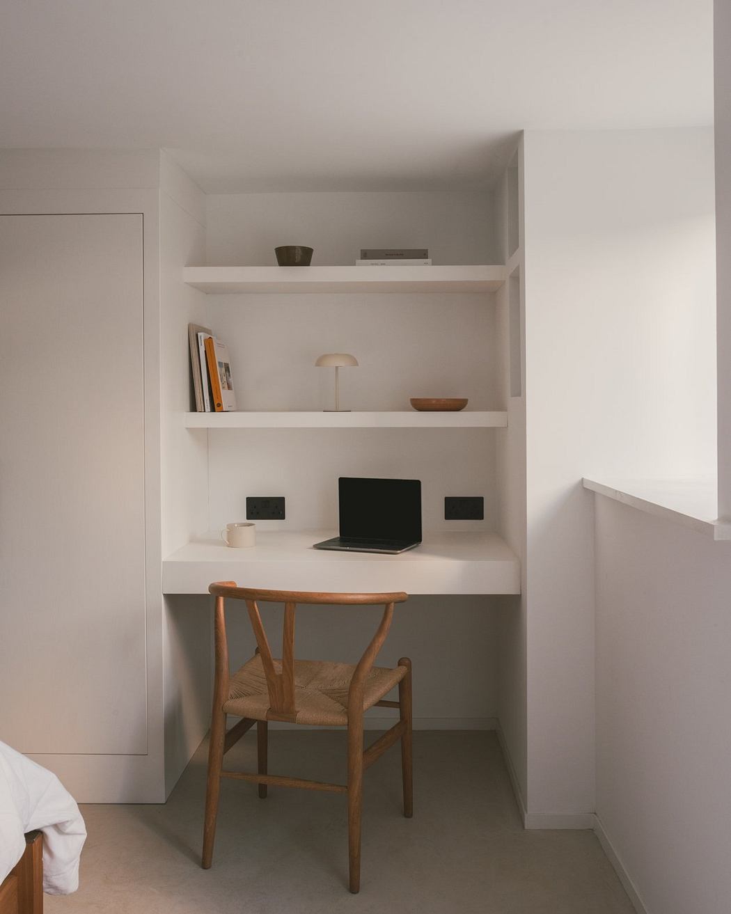 A minimalist built-in desk nook with shelves, a laptop, and a wooden chair.