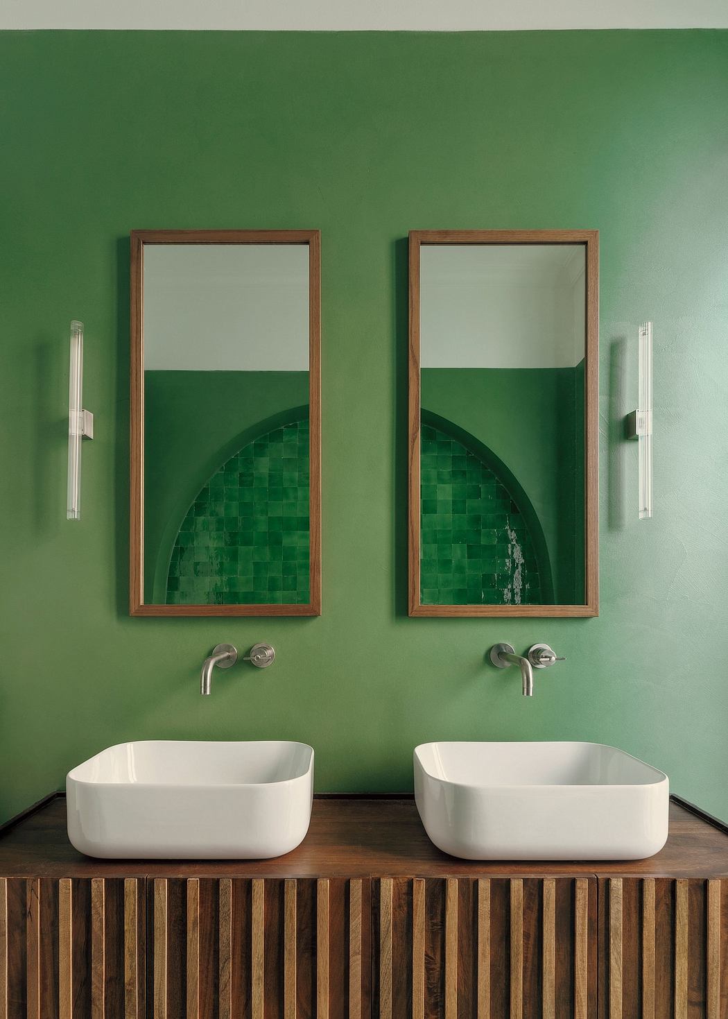 Minimalist bathroom with wooden vanity, vessel sinks, and green tiled wall.