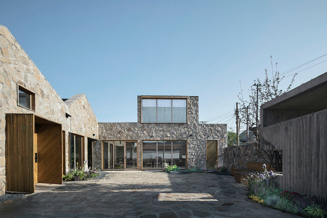 Modern stone-and-wood building with large windows, surrounded by a paved courtyard and landscaping.