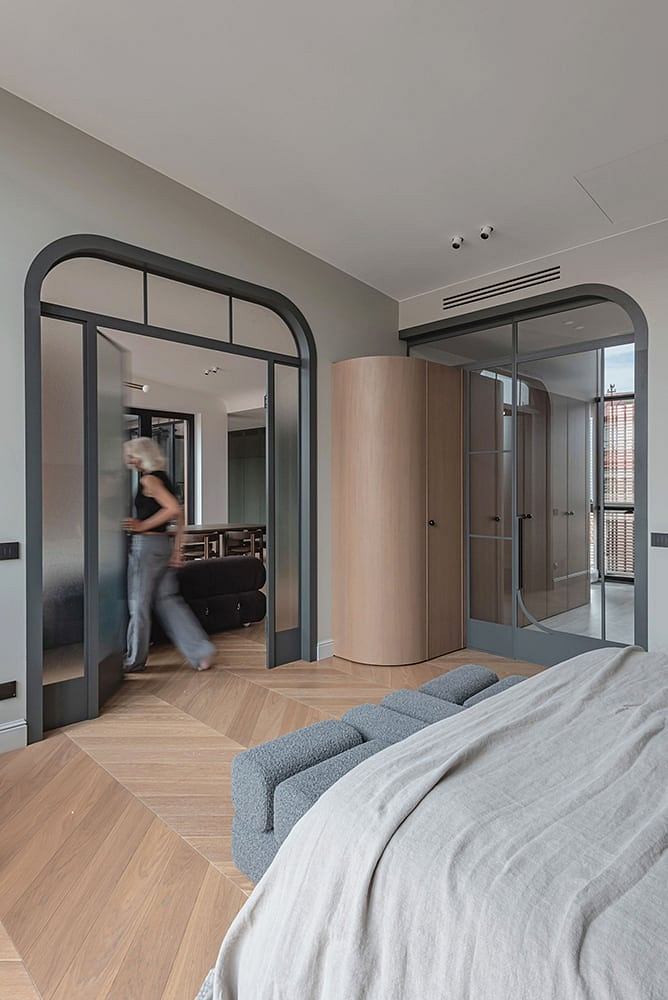 Sleek modern bedroom with arched doorframes, wood floors, and a cozy seating area.
