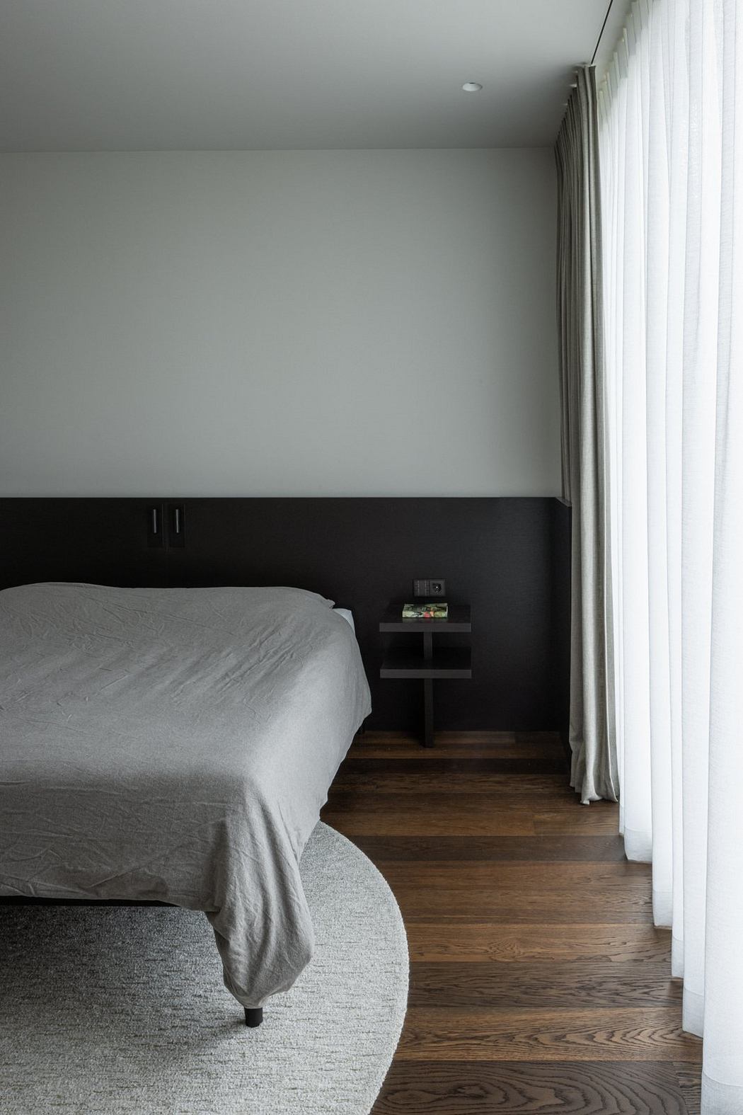 Minimalist bedroom with wood flooring, black accent wall, and subtle lighting details.