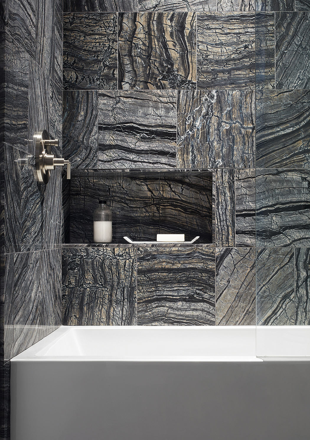 Exquisite marble wall panels, minimalist white bathtub, and built-in shelving highlight the modern, sleek design.