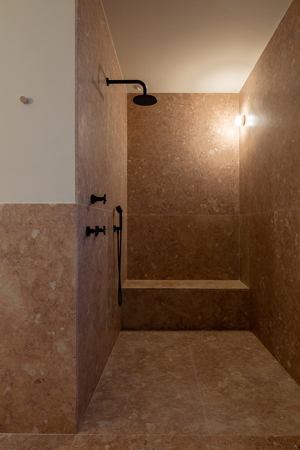 A spacious shower stall with natural stone tiles and a modern black shower head.