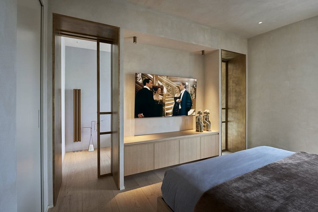 A modern bedroom with a large TV display, minimalistic furniture, and warm lighting.