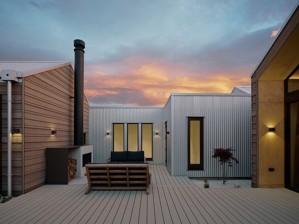 A modern rustic outdoor deck at sunset, featuring corrugated metal siding, wooden benches, and a chimney.