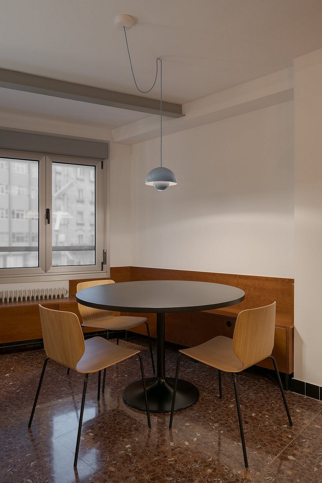 A modern dining area with a round table, wooden chairs, and a pendant light fixture.