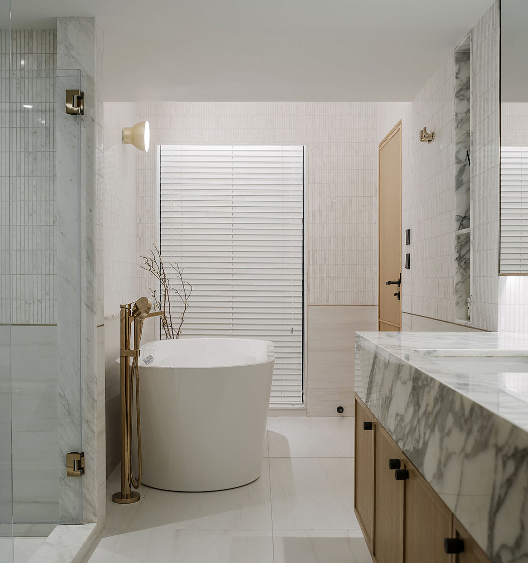 Modern, minimalist bathroom with marble countertops, freestanding tub, and white tile walls.
