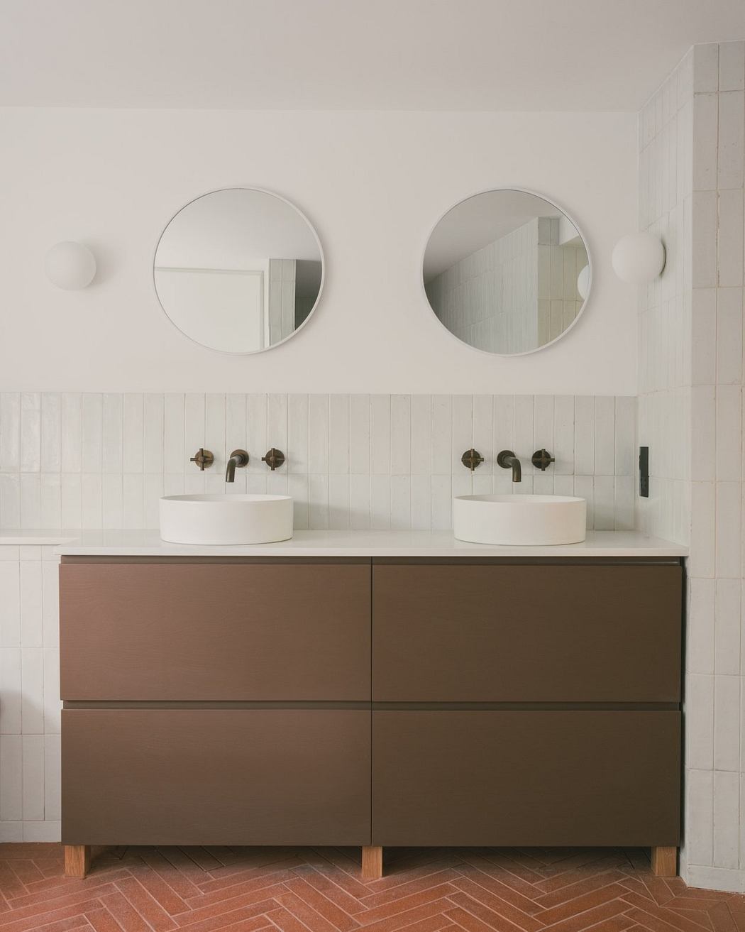 Minimalist bathroom with circular mirrors, vessel sinks, and a wooden vanity cabinet.