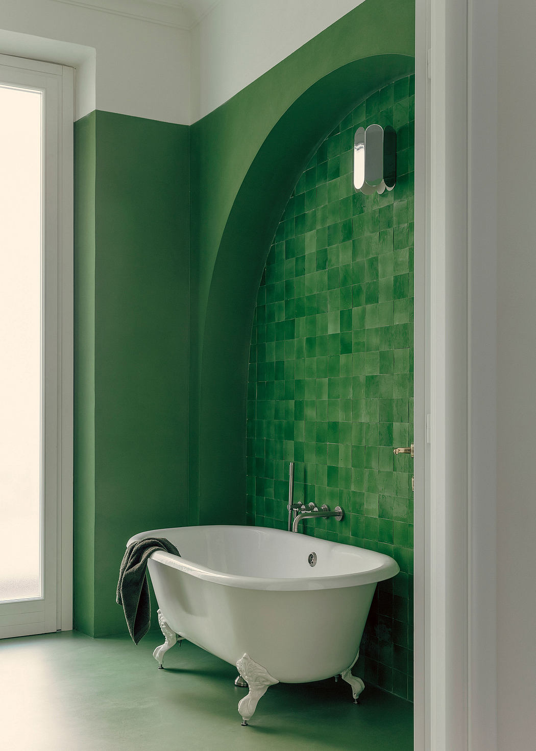 A modern bathroom with a white clawfoot tub and striking green mosaic tile walls.