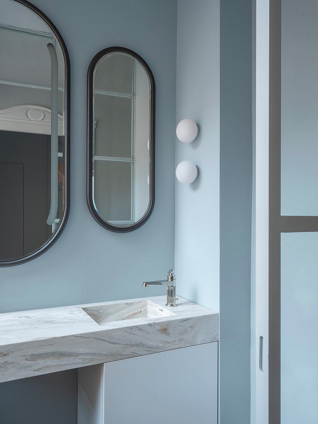 Minimalist bathroom design with oval mirrors, marble vanity, and modern lighting.