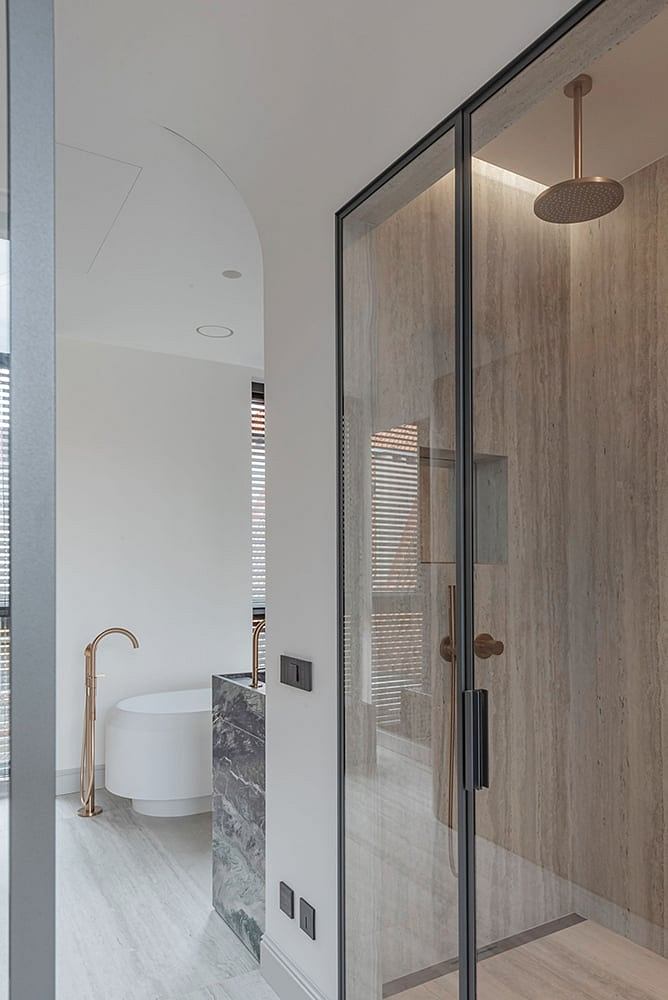 A modern bathroom with a glass shower enclosure, wood paneling, and brass fixtures.