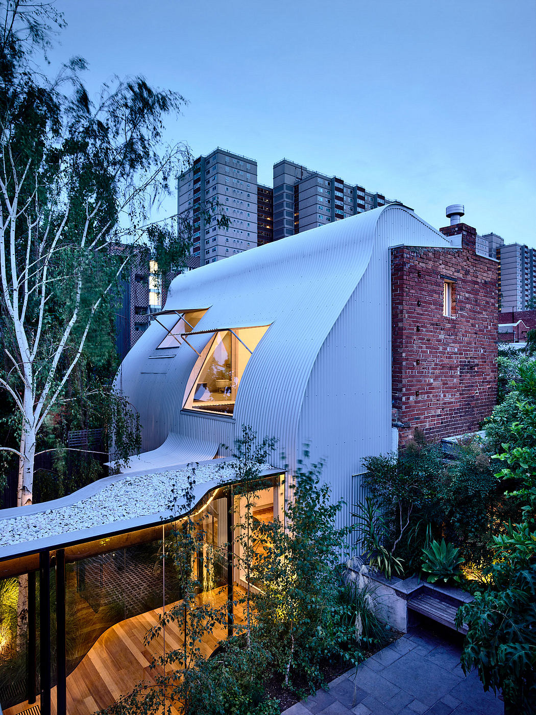 Curved corrugated metal roof and brick facade of a modern urban home nestled among trees.