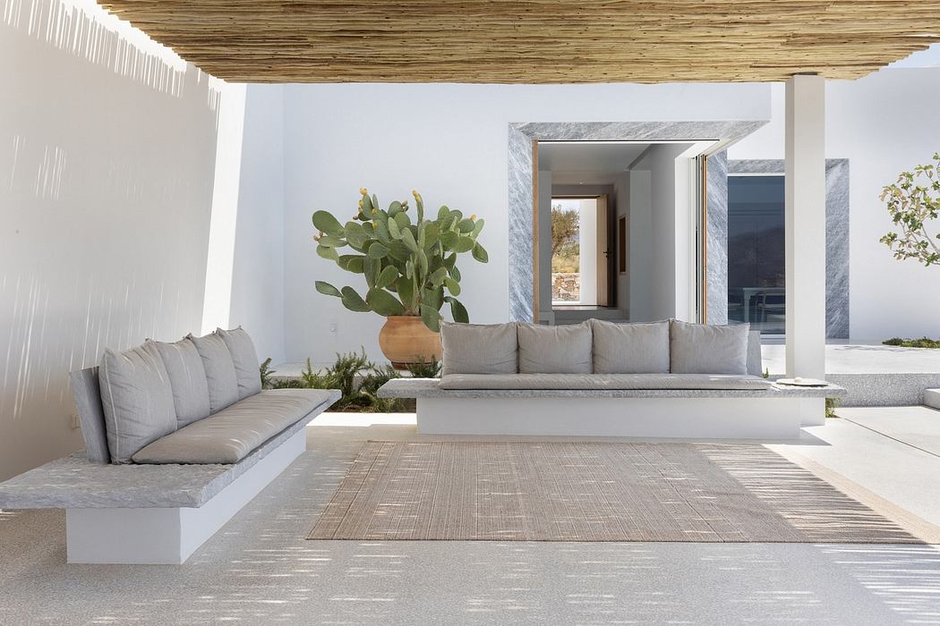 Minimalist patio design with plush seating, potted plants, and wood-slat canopy overhead.