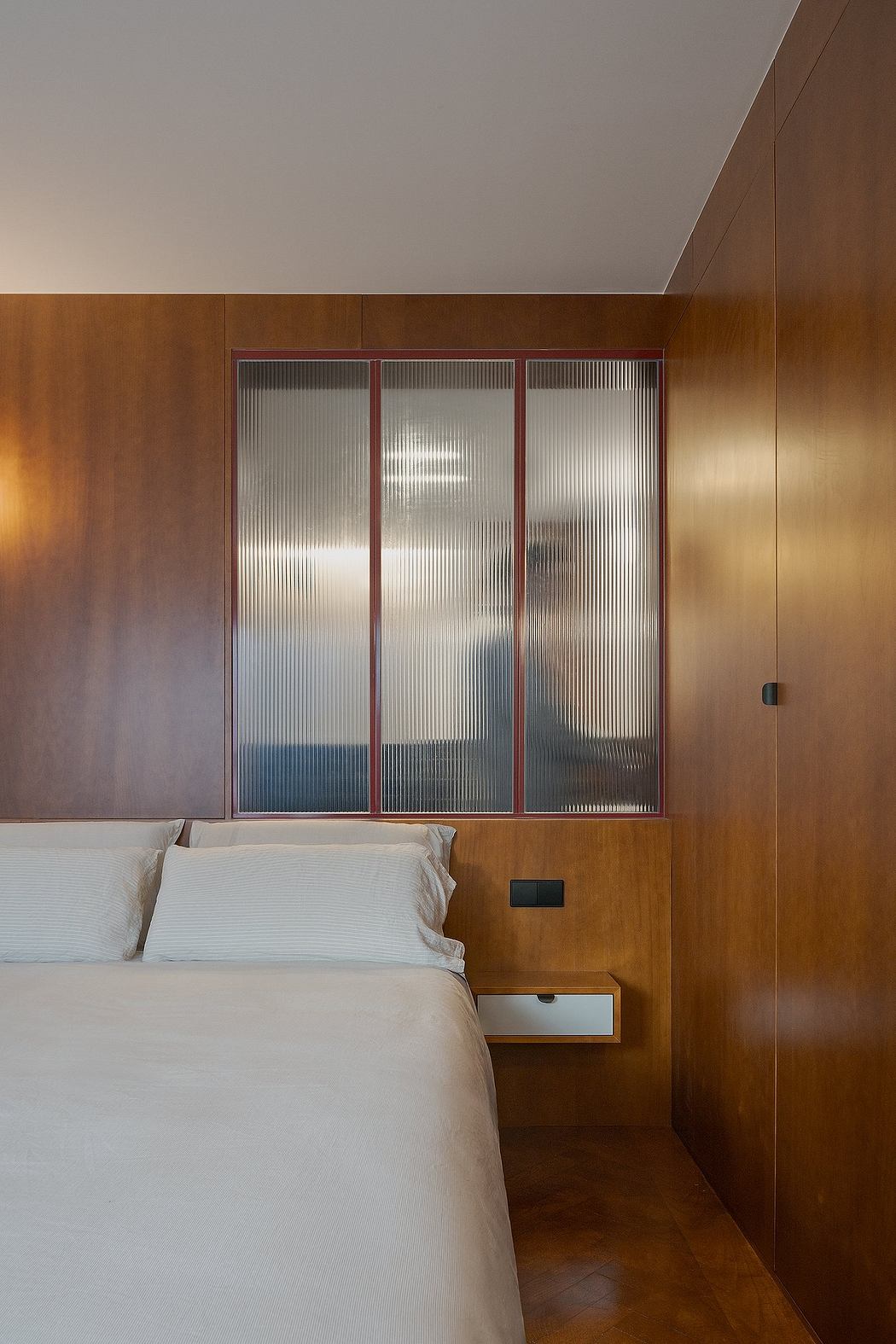 Warm-toned wood paneling, ribbed glass windows, and minimalist bedside table.