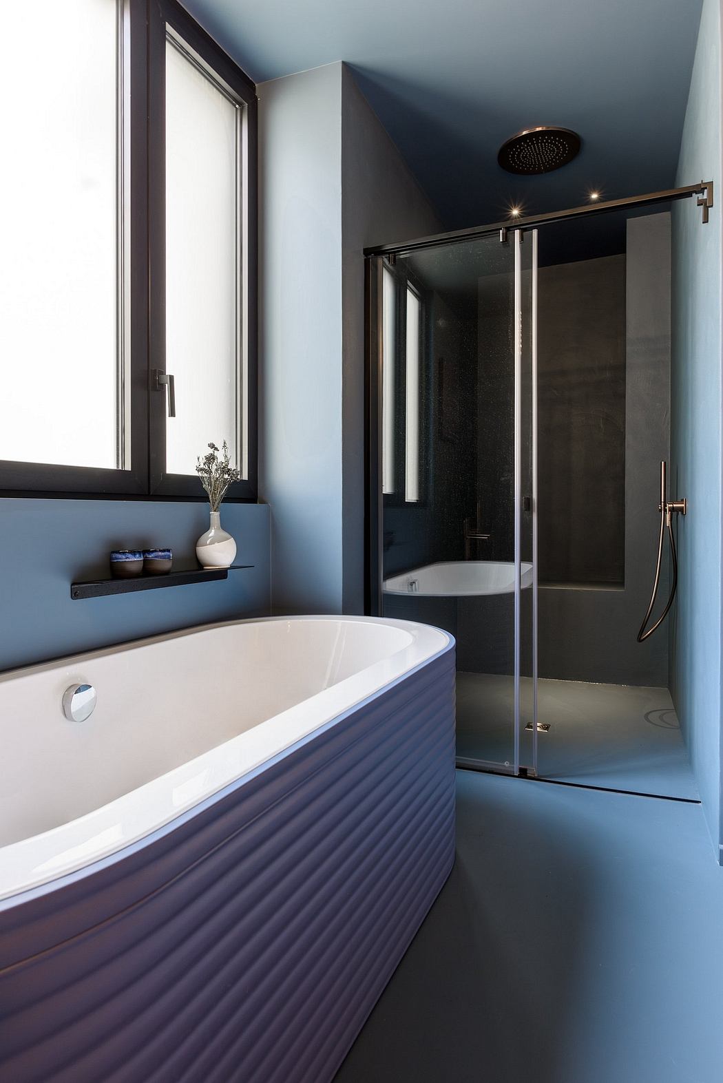 A modern bathroom with a white freestanding bathtub, glass shower enclosure, and dark accents.
