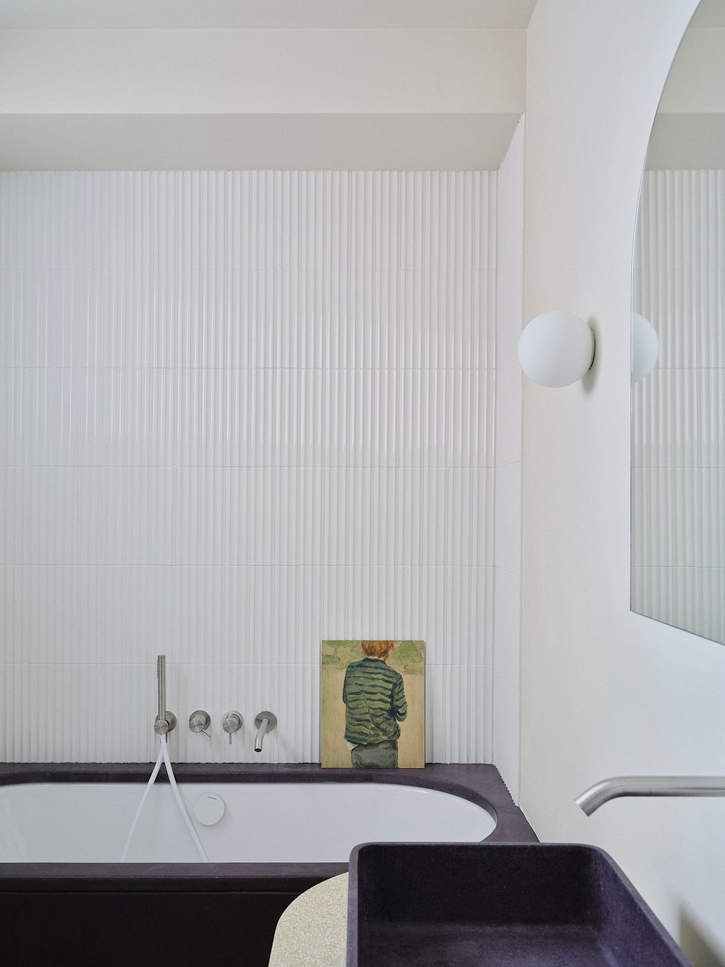 A modern, minimalist bathroom with vertical tile patterns, a black vanity, and a wall-mounted artwork.