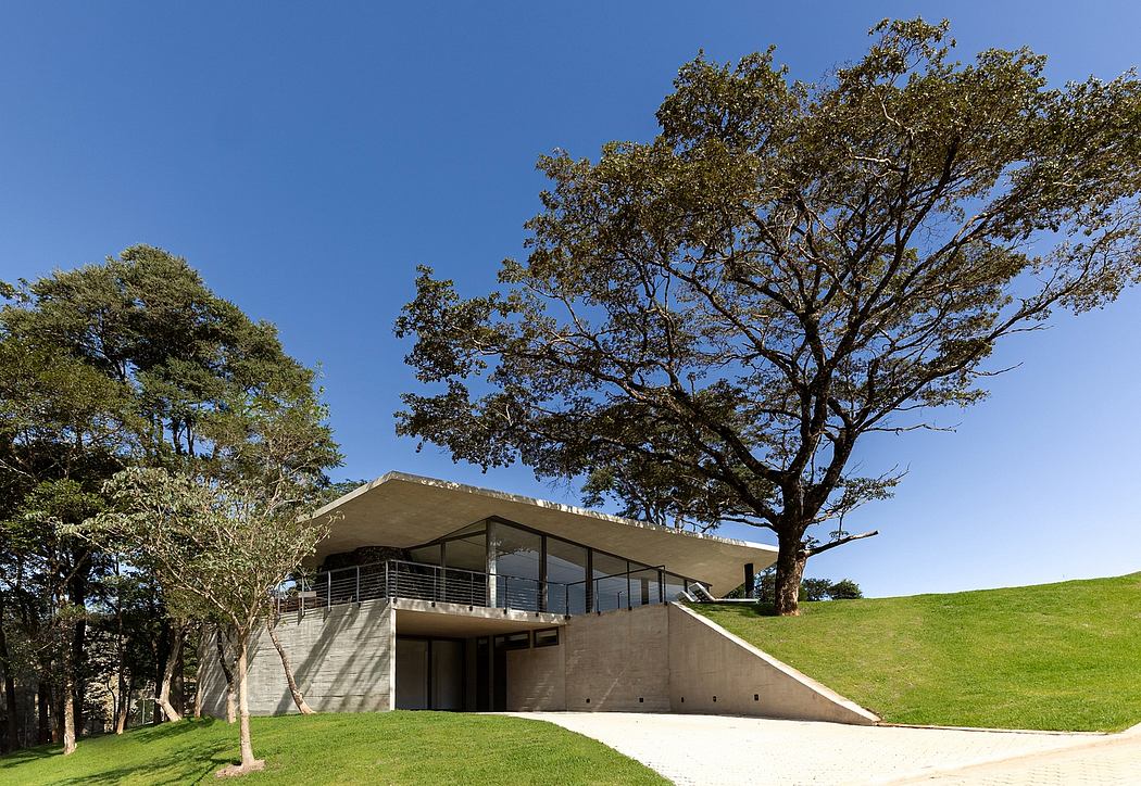 A modern concrete building with a sloping roof and balconies, surrounded by lush greenery.