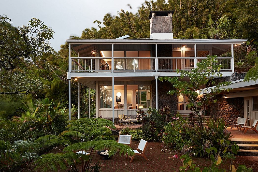 A multi-level wooden and stone house surrounded by lush tropical foliage, with outdoor seating areas and warm interior lighting.