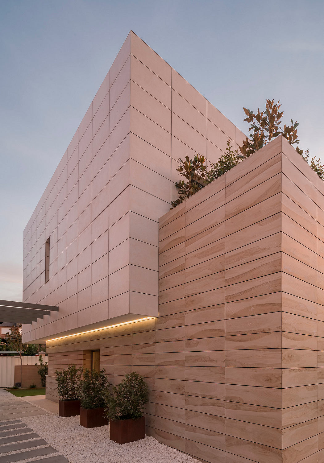 A modern building with a geometric facade, featuring wooden paneling and strategic lighting.