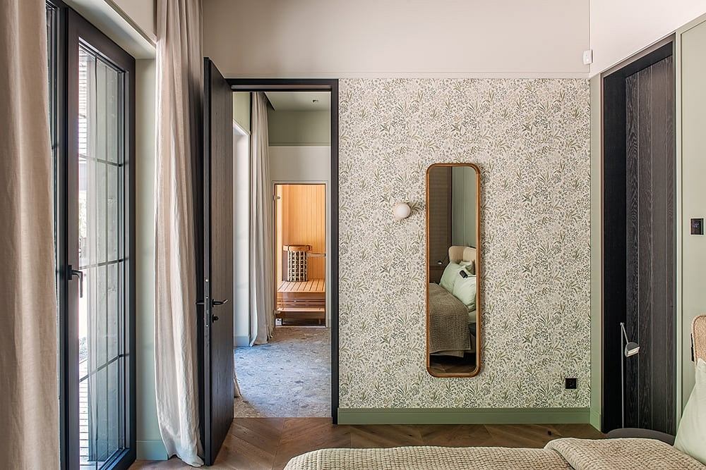 Stylish bedroom with patterned wallpaper, wooden floors, and large framed mirror.