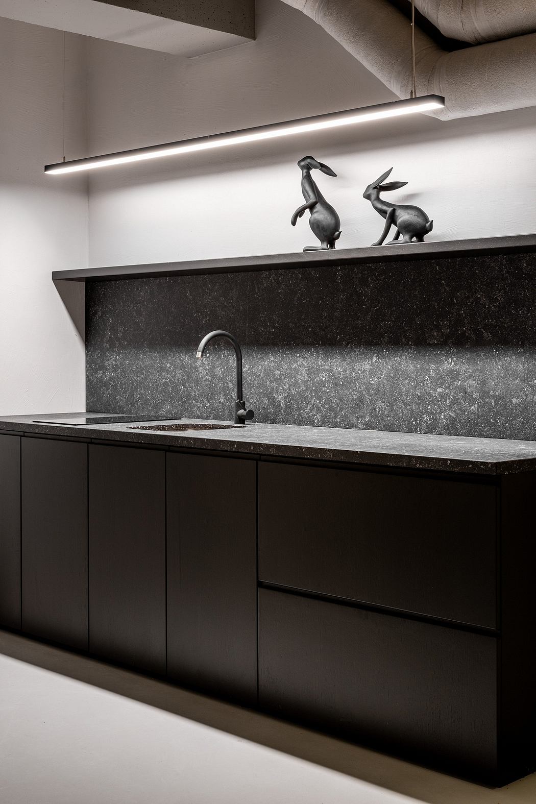 Modern kitchen design featuring sleek dark cabinetry, a black stone countertop, and minimalist decorative sculptures.