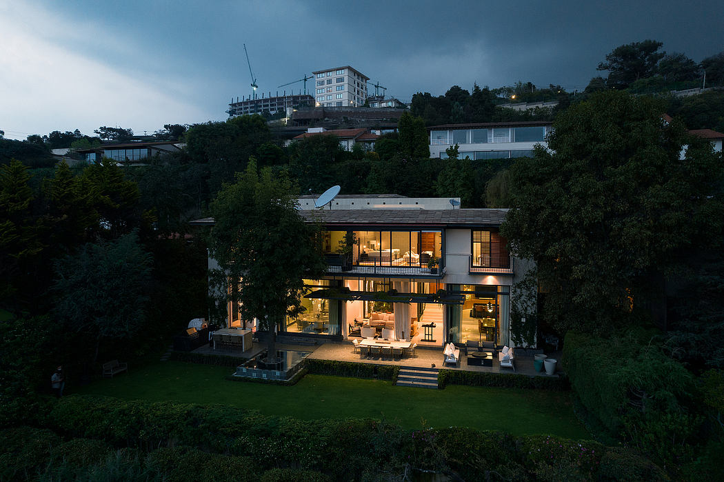 Striking modern house with illuminated interior, surrounded by lush greenery.