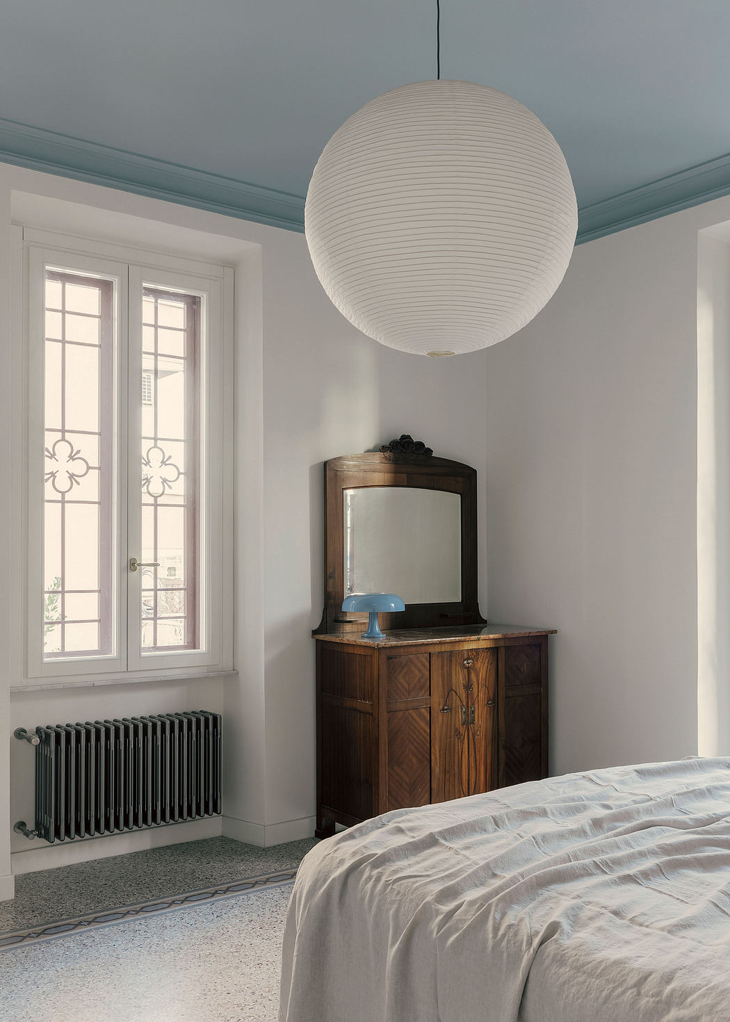 A cozy bedroom with a large, illuminated globe pendant, wood furnishings, and patterned windows.
