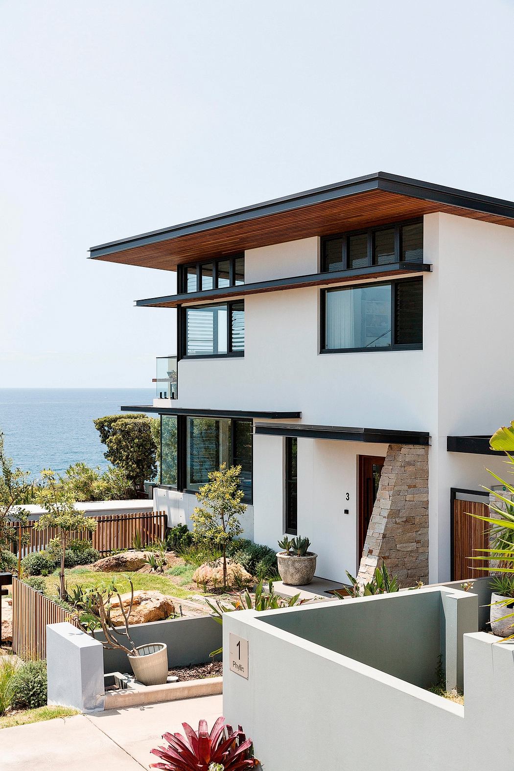 Contemporary coastal home with sleek wood-accented exterior, expansive windows, and lush landscaping.