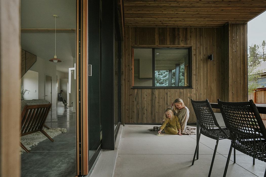 A modern, wooden interior with concrete floors, chairs, and a person sitting on the floor.
