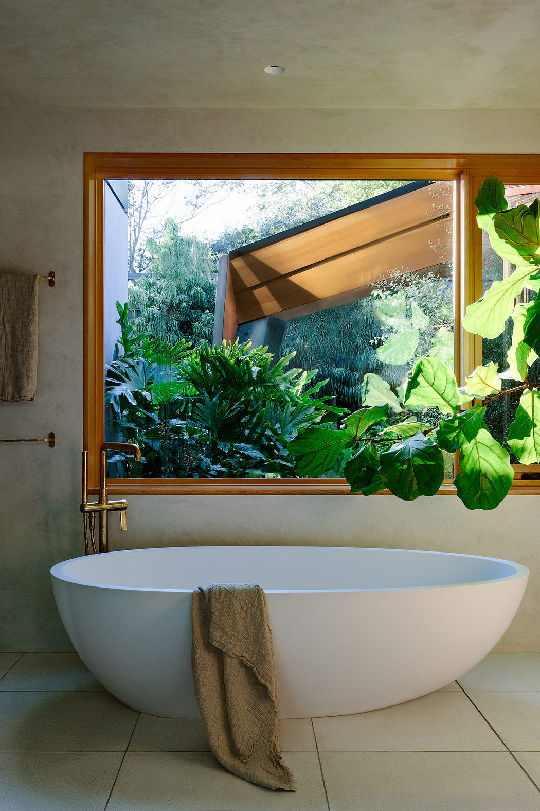 A modern bathroom with a white bathtub, wooden frame window, and lush greenery outside.