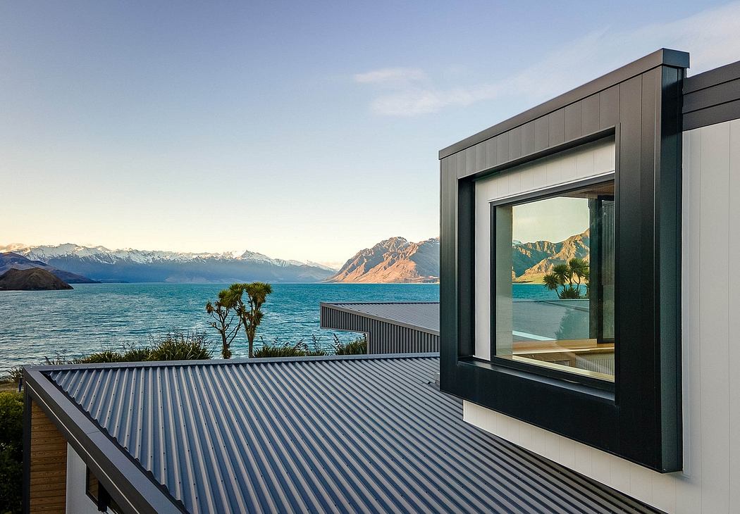 Modern exterior with glass windows overlooking a scenic lake and snow-capped mountains.