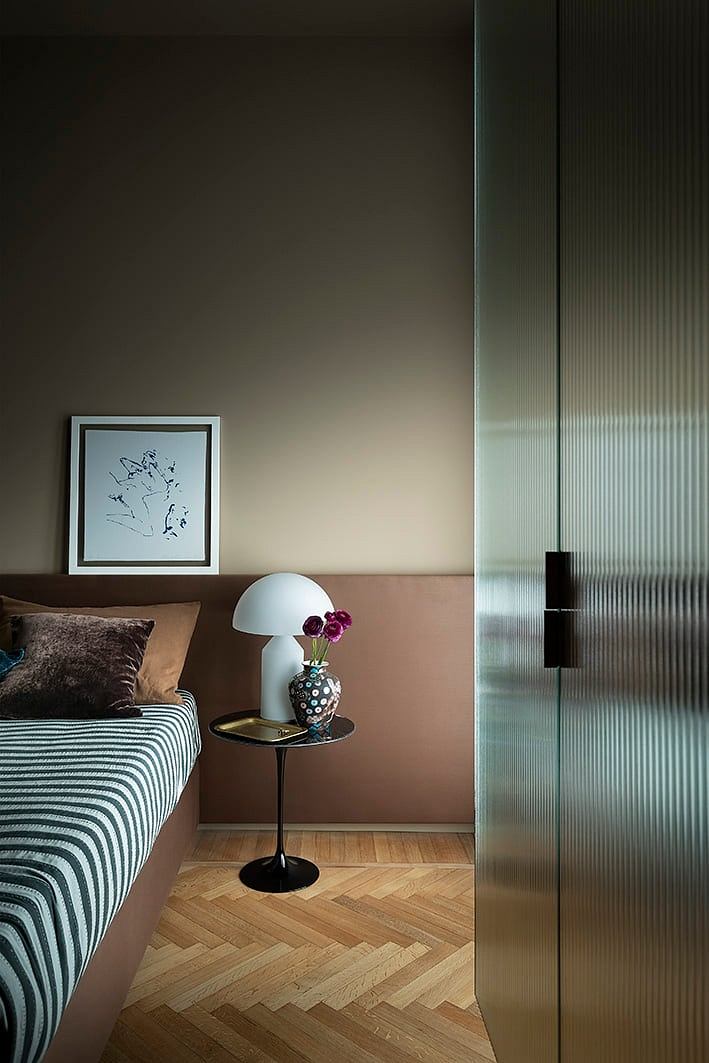 Cozy bedroom with striped bedding, framed artwork, and a glass partition providing visual interest.