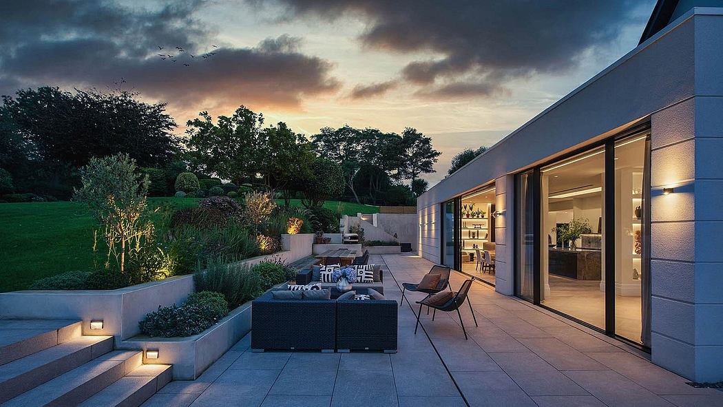 Modern home patio with cozy seating area, landscaped gardens, and dramatic evening sky.
