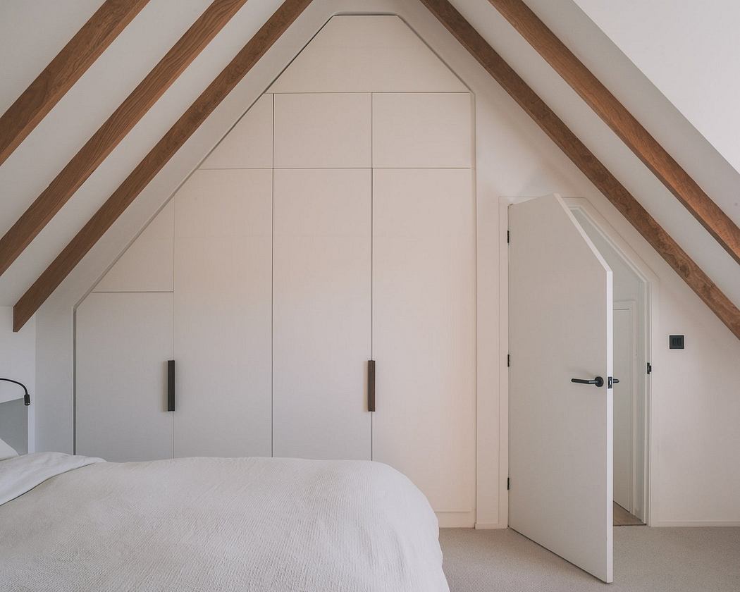 Minimalist bedroom with wooden beams and built-in closets under attic roof.