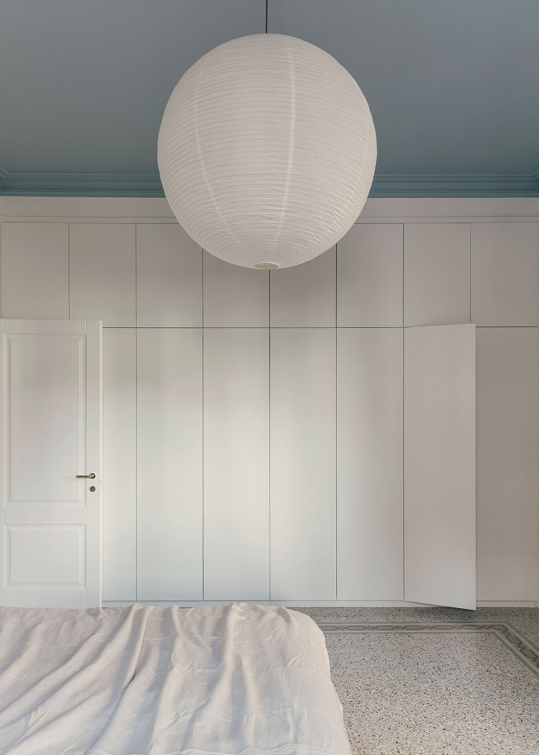 A minimalist, bright bedroom with a large, round paper lantern light fixture.