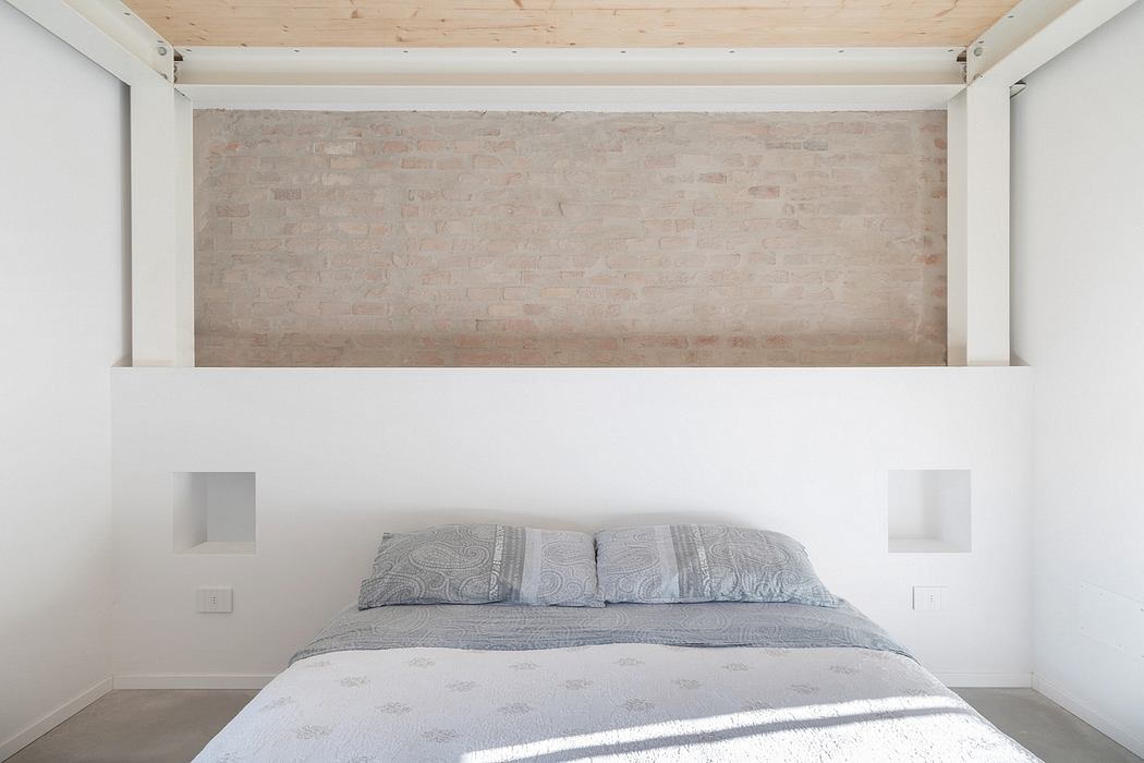 Minimalist bedroom with exposed brick wall, wooden ceiling, and simple furnishings.