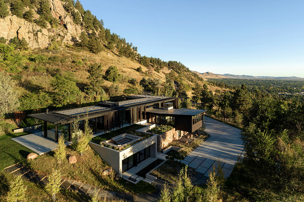 A modern, hillside residence with expansive windows, terraces, and a natural, wooded setting.