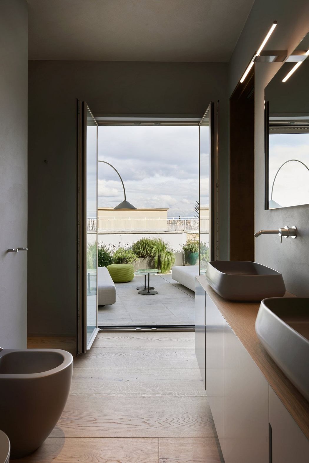 Sleek modern bathroom with large glass doors opening to a terrace and skyline.