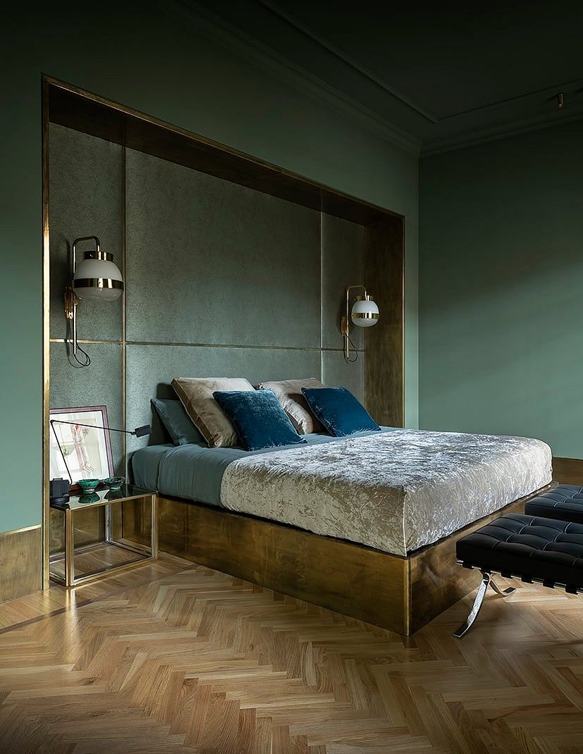 Elegant bedroom with dark green walls, brass-framed bed, and herringbone wood flooring.