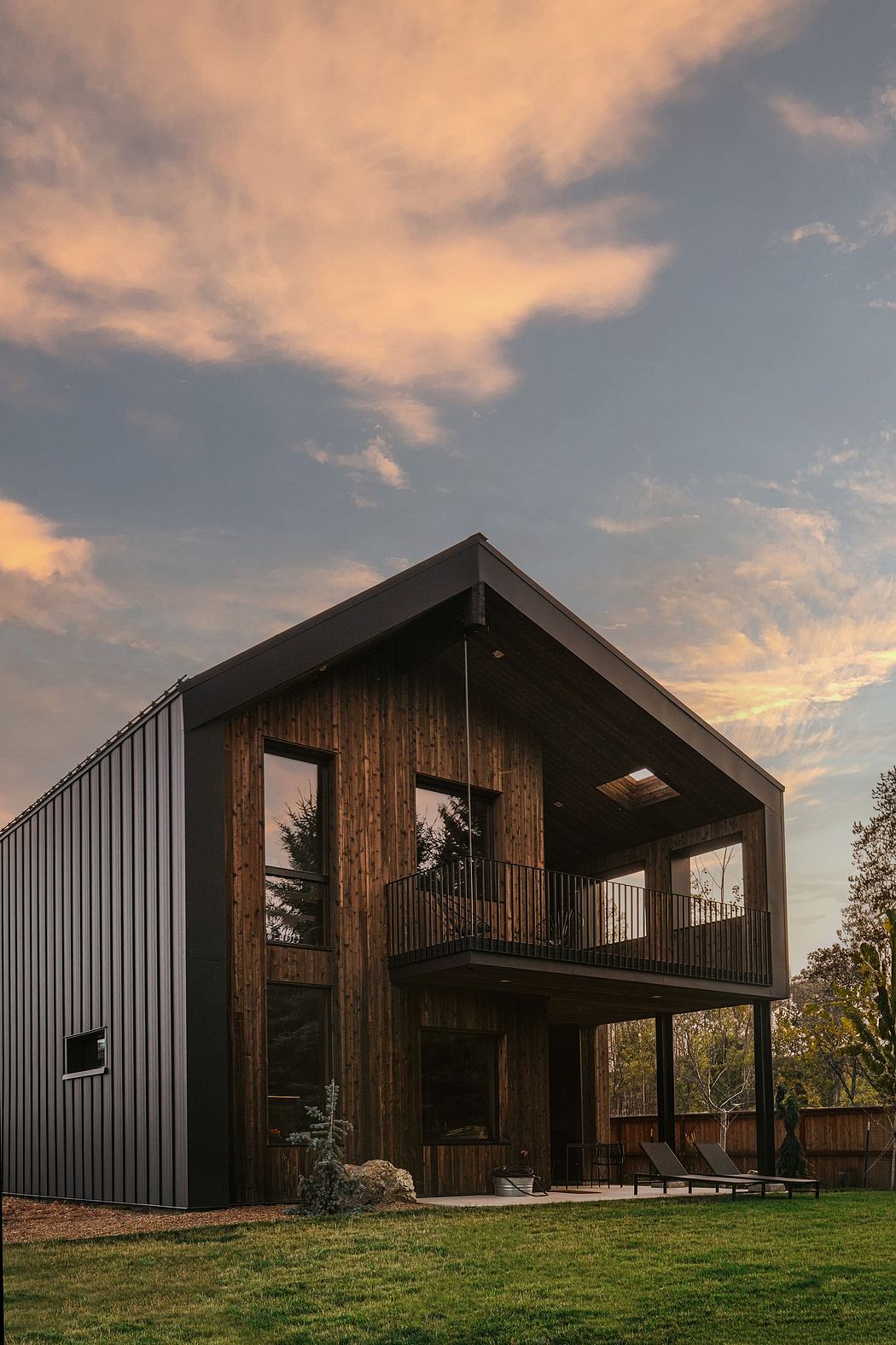 A modern, two-story cabin with a wooden exterior, wraparound balcony, and dramatic sky.
