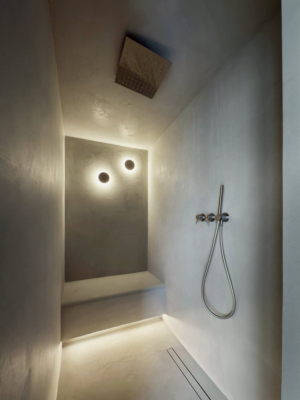 A modern, minimalist shower area with recessed lighting and a sleek, chrome shower head.