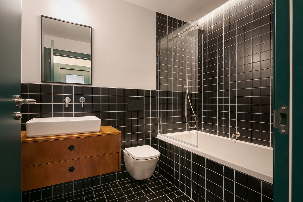 A bathroom interior with black tile walls, a wood vanity, and a bathtub with a shower.