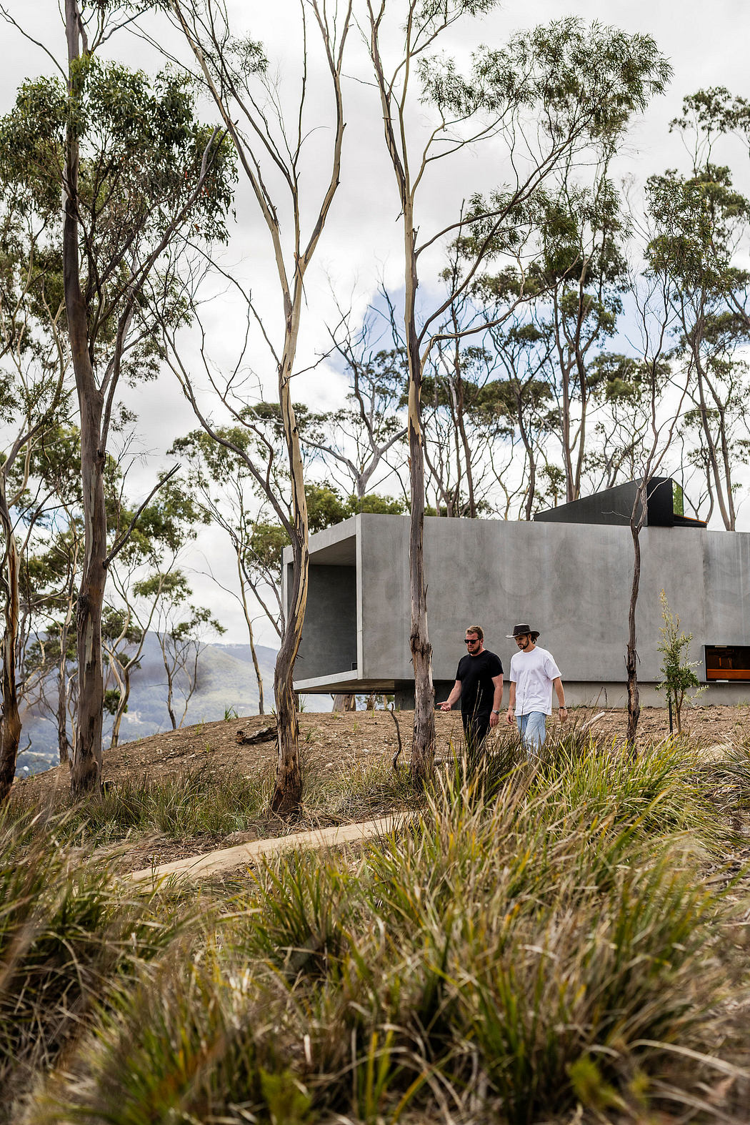 A modern concrete structure amid the lush, forested landscape, with two people walking along the path.