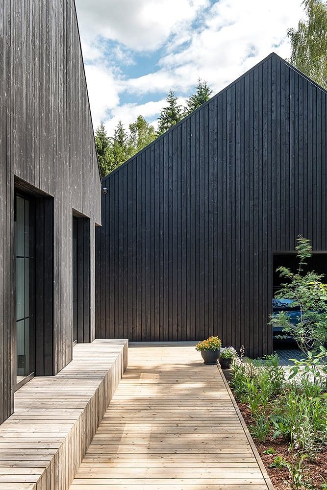 Wooden walkway leading to modern black wood-paneled building with large windows.