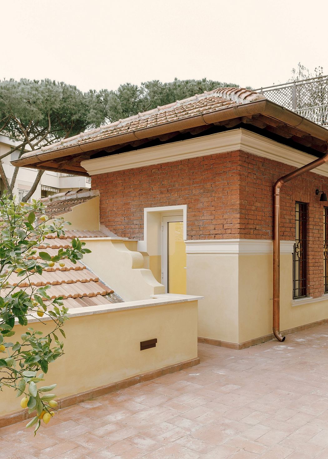 Brick exterior with tiled roof, white trim, and leaf-covered tree branches.