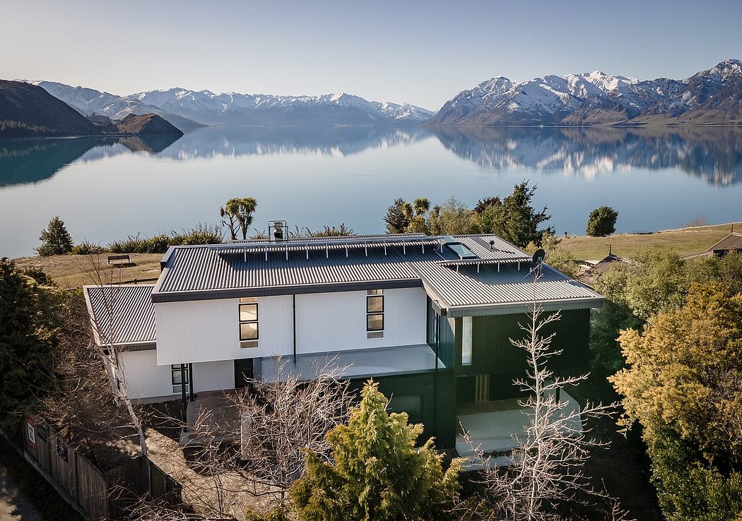 A modern, multi-story home nestled among trees with a stunning lake and mountain view.