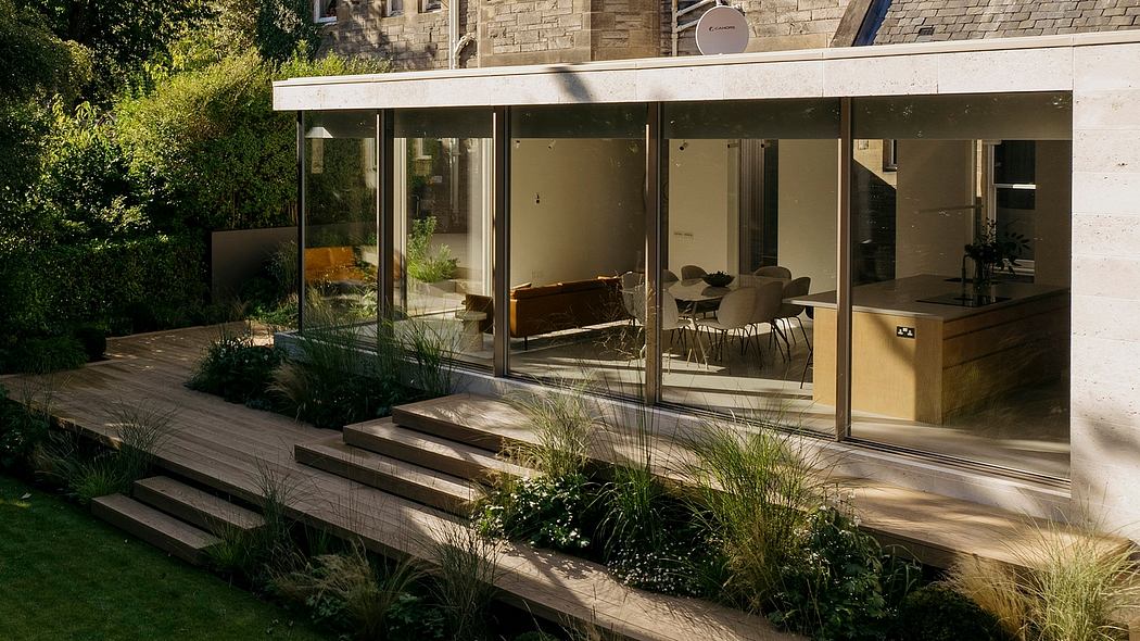 A modern glass-walled house extension with a wooden deck and lush garden landscaping.